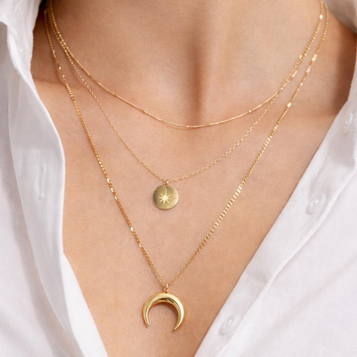 Close up of a person wearing two gold necklaces with star and crescent moon pendants on a white shirt background