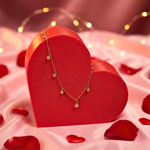 Load image into Gallery viewer, Gold necklace on a red heart-shaped box with red petals and string lights in the background