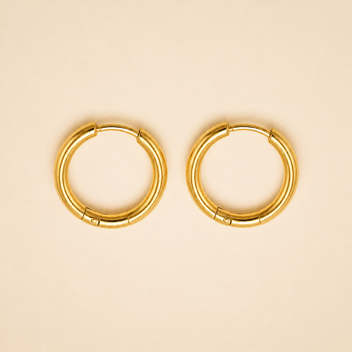 A pair of gold plated circular hoop earrings with a segmented, tubular design, displayed on a solid light beige background